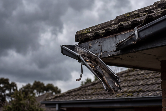 Storm-damaged gutter, dark clouds (Insurance & Storm Repairs): "Storm-damaged guttering hanging loose from a roof edge, insurance repair work by Peak Property Maintenance